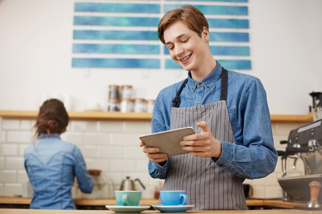 Cajero masculino tomando pedidos usando la pestaña en la cafetería brillante.