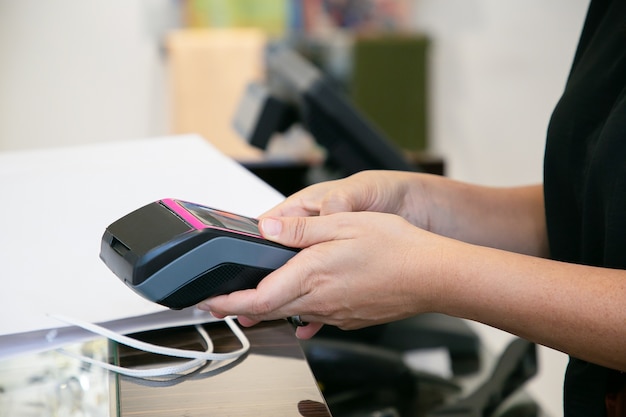 Cajero o vendedor operando el proceso de pago con terminal pos y tarjeta de crédito. Toma recortada, primer plano de las manos. Concepto de compra o compra