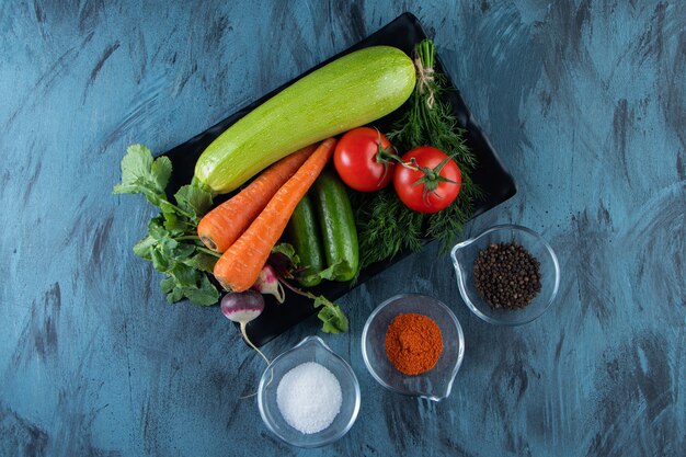 Calabacín fresco, zanahoria, tomate y verduras en un plato negro con especias.