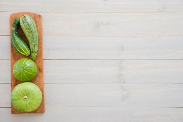 Calabacín; Pepino y calabaza en la tabla de cortar sobre el escritorio de madera blanco