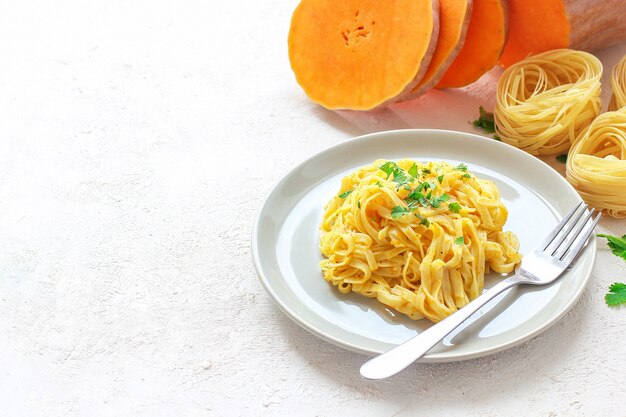 Calabaza Alfredo fettucine pasta en un plato de cerámica con rodajas de calabaza cruda fresca. Comida de otoño para el almuerzo. Receta de calabaza moscada.