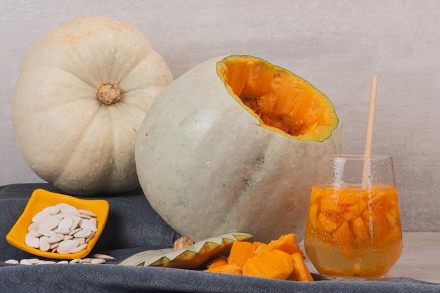 Calabaza blanca, vaso de jugo y semillas de calabaza en el cuadro blanco.