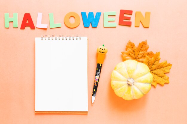 Calabaza y hojas cerca de la escritura y papelería de Halloween