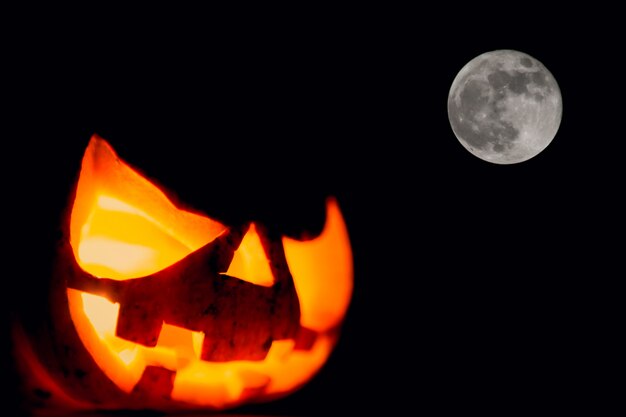 Calabaza con luz dentro en un fondo oscuro y la luna al lado