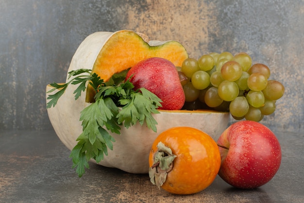 Foto gratuita calabaza con manzanas y uvas en la pared de mármol.