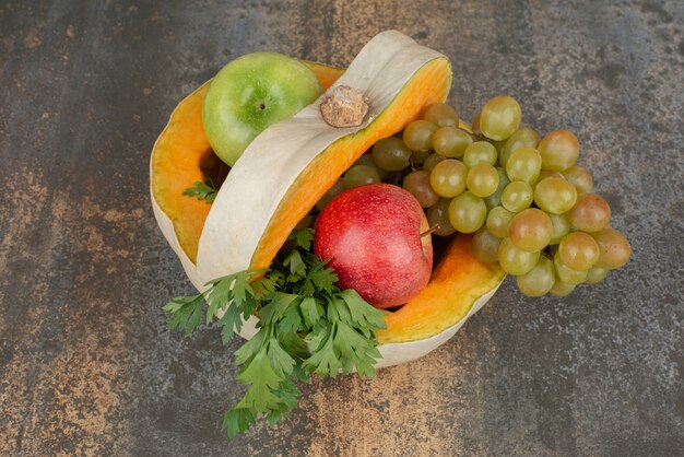 Calabaza con manzanas y uvas sobre superficie de mármol.