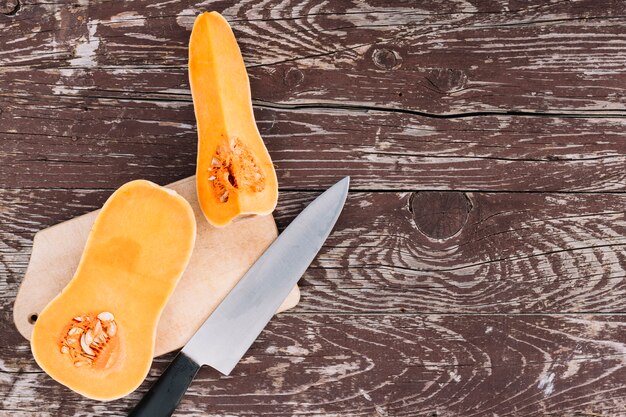 Calabaza de naranja orgánica cruda en la tabla de cortar con un cuchillo sobre el escritorio de madera