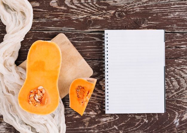 Una calabaza orgánica sobre tela y tabla de cortar con cuaderno de espiral en el escritorio de madera