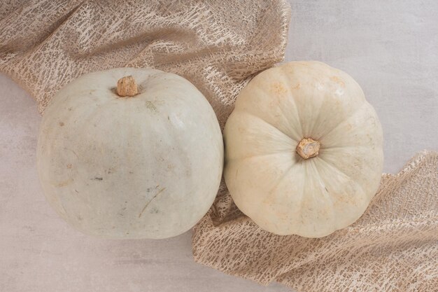 Calabazas maduras blancas sobre mesa blanca con arpillera.