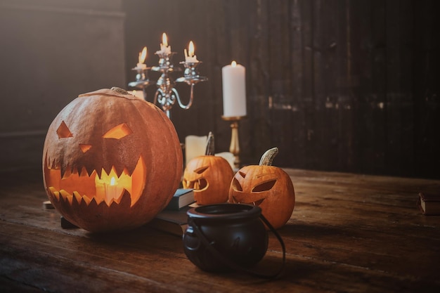 Calabazas talladas tradicionales de Halloween, pequeña caldera y velas en el suelo de madera.