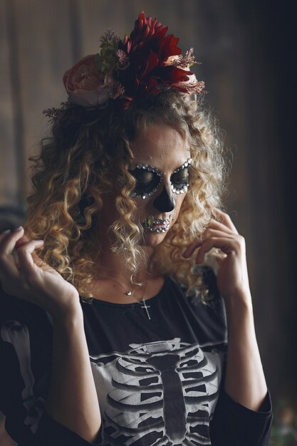 Calavera de maquillaje de Halloween hermosa mujer con peinado rubio. Niña modelo Santa Muerte en traje negro.