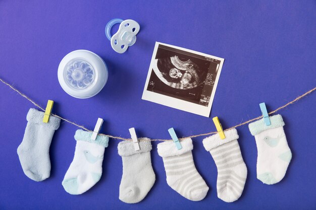 Calcetín de bebé colgado en el tendedero con biberón; Imagen de chupete y ultrasonido sobre fondo azul.
