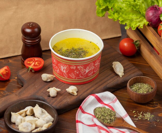 Caldo de pollo con sopa de hierbas en un tazón de taza desechable servido con verduras verdes.