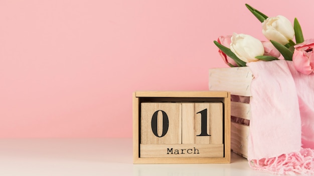 Foto gratuita calendario de madera con 1 de marzo cerca de la caja con tulipanes y bufanda en el escritorio con fondo rosa