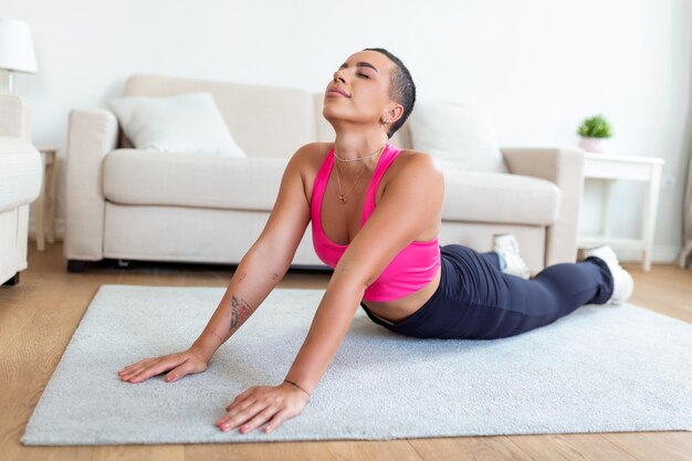 Calentamiento antes del entrenamiento Sonriente mujer negra deportiva entrenando en casa o en el estudio del club de fitness Hermosa mujer estirando las piernas después de los ejercicios en la alfombra