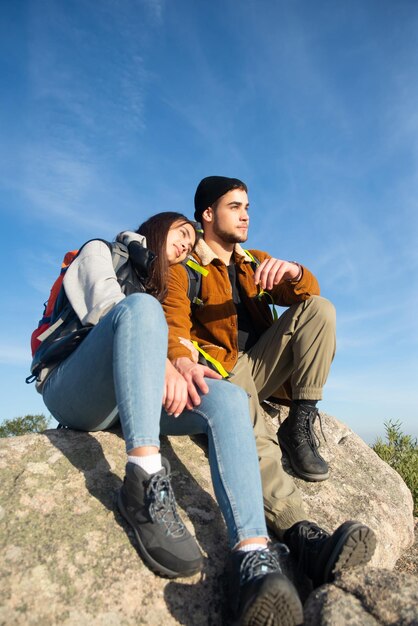 Cálida pareja de senderismo en otoño. Hombre y mujer sentados en el pico, novia apoyada en el hombro. Amor, ocio, concepto de relación.