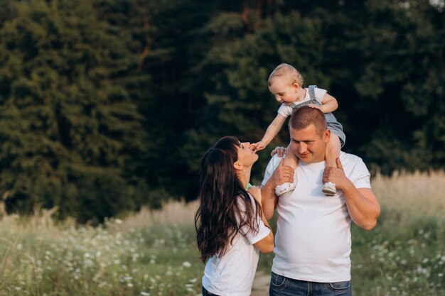 Cálidos abrazos de padres jóvenes y su pequeña hija de pie en el campo de verano