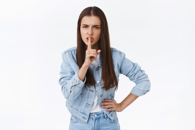 Foto gratuita cállate chica morena de aspecto serio, enojada y enojada, que se calla ante la cámara con una expresión de indignación, exige silencio o silencio, presiona el dedo índice en los labios con un gesto de shhh regañando a alguien