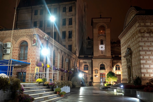 Calle peatonal de noche con iluminación, iglesias, edificios, vegetación y flores en Bucarest, Rumania