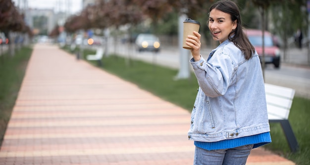 Calle retrato de una mujer joven alegre en un paseo con café en un espacio de copia de parque borrosa.