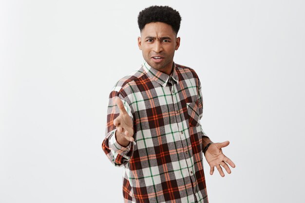 Calmate hermano. Retrato de un confuso joven africano guapo de piel negra con cabello rizado en camisa casual a cuadros, gesticulando con las manos, confundido por su amigo tratando de golpearlo.