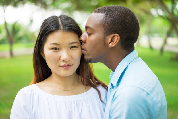 Calme a la muchacha china hermosa que siente beso del novio y que mira la cámara.