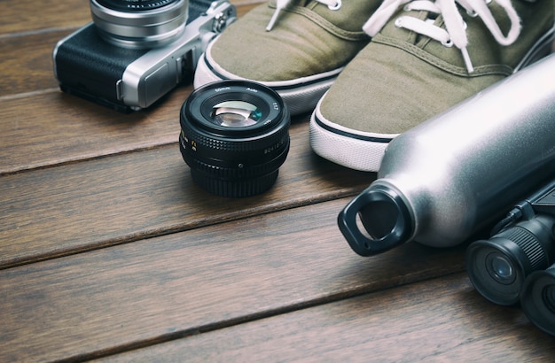 Cámara, lente, binocular, zapatos de lona, ​​botella de deportes en la mesa de madera retro