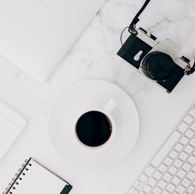 Camara vintage teclado; Taza de café y diario sobre fondo de mármol blanco