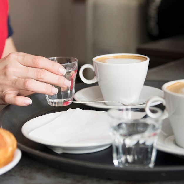 Camarera colocando un vaso de agua con café en la bandeja