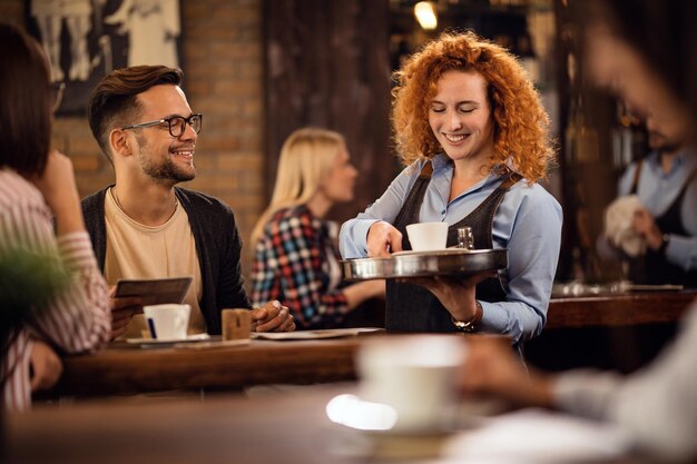 Camarera feliz dando café a los clientes mientras les sirve en la cafetería