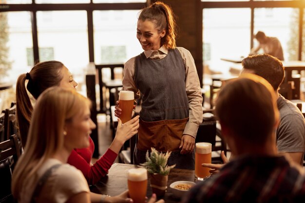 Camarera feliz sirviendo cerveza a un grupo de jóvenes en un pub