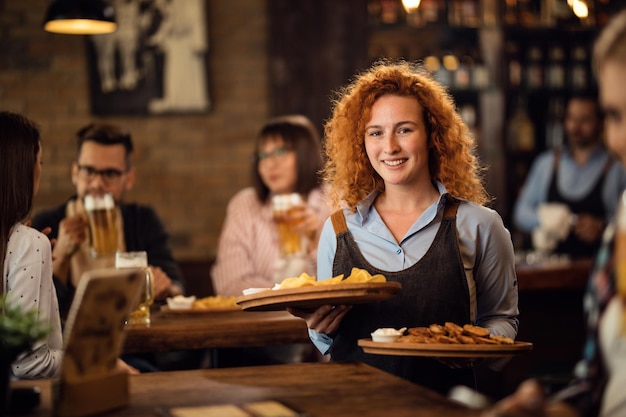 Una camarera pelirroja feliz sirviendo a los clientes en un restaurante y trayendo comida a su mesa