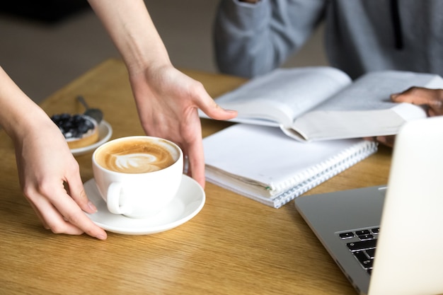 Camarera que sirve capuchino para el visitante de la cafetería en la mesa del café, primer plano