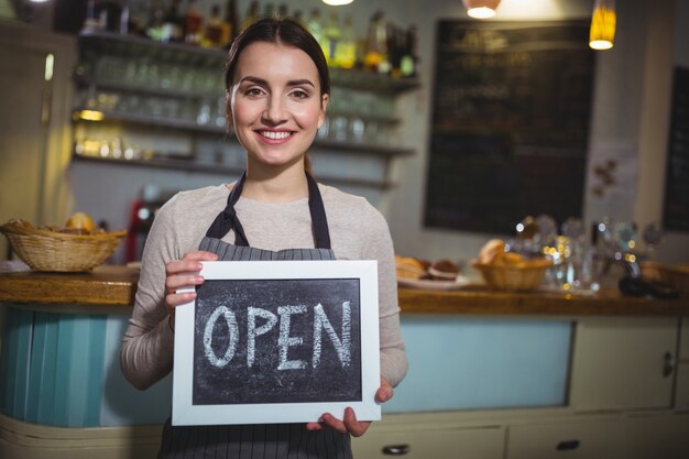 Camarera sonriente que muestra la pizarra con la muestra abierta en la cafetería ©