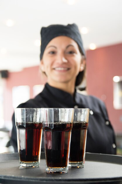 Camarera sonriente sosteniendo vasos de bebidas alcohólicas