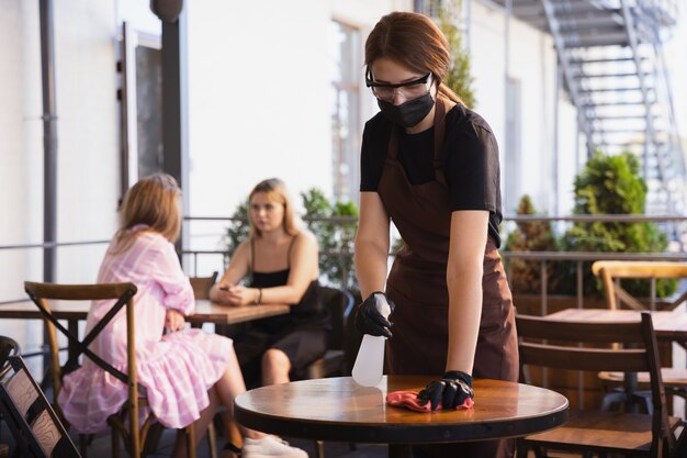 la camarera trabaja en un restaurante con una máscara médica, guantes durante la pandemia de coronavirus