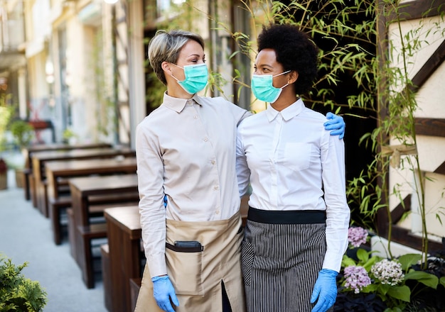 Camareras felices con máscaras protectoras y guantes mientras trabajan en un café al aire libre