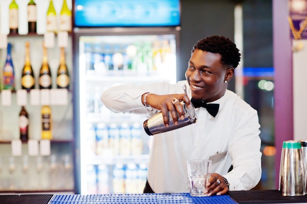 Camarero afroamericano en el bar con agitador Preparación de bebidas alcohólicasxA