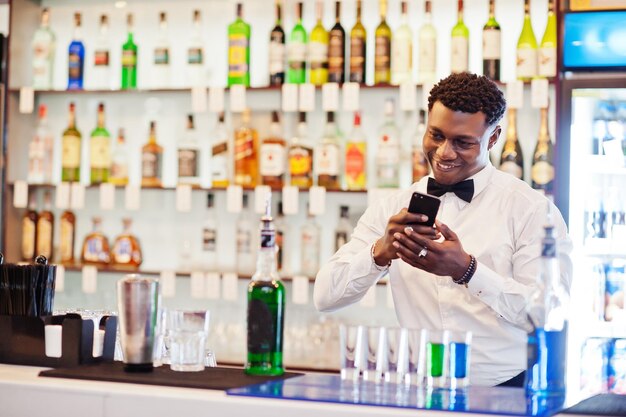 Camarero afroamericano en el bar haciendo cócteles en tomas y tomando fotos en el teléfono Preparación de bebidas alcohólicasxA