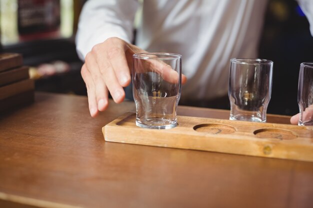 Camarero arreglando el vaso de cerveza en la bandeja en la barra de bar