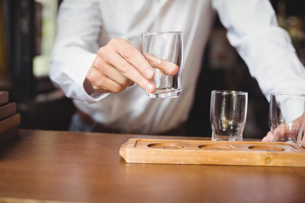 Camarero arreglando el vaso de cerveza en la bandeja en la barra de bar