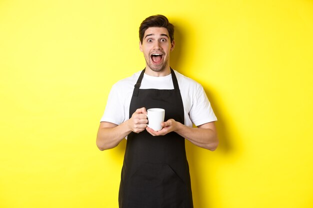 Camarero de cafetería amigable de pie con las manos levantadas, lugar para su cartel o logotipo, de pie sobre fondo amarillo.