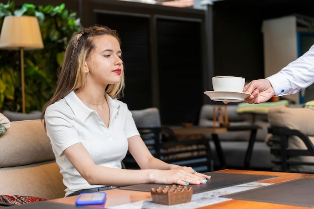 Un camarero dando una taza de café a la joven en el restaurante.