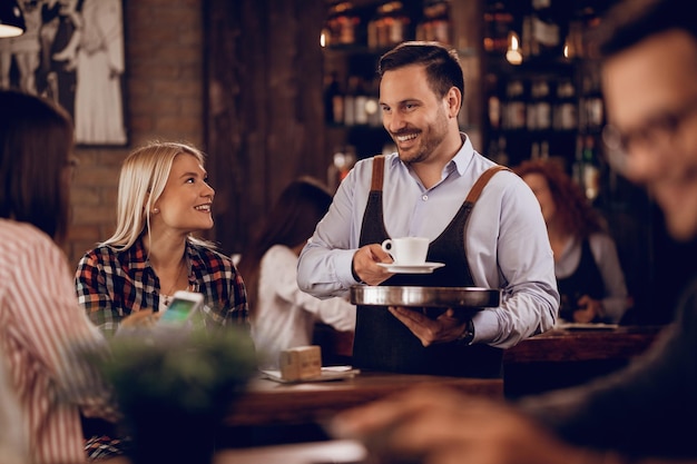 Camarero feliz comunicándose con los clientes mientras les sirve café en un pub