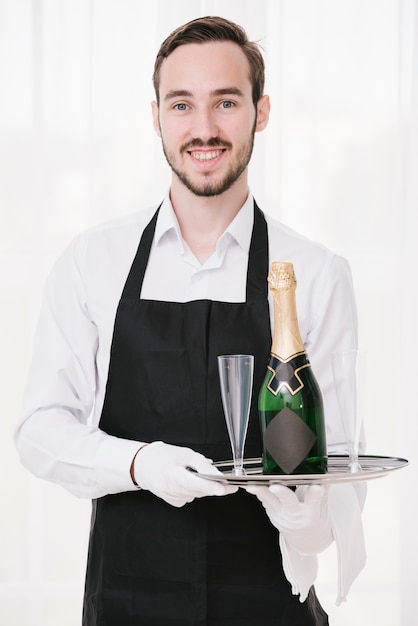 Camarero feliz que sostiene la bandeja con champán