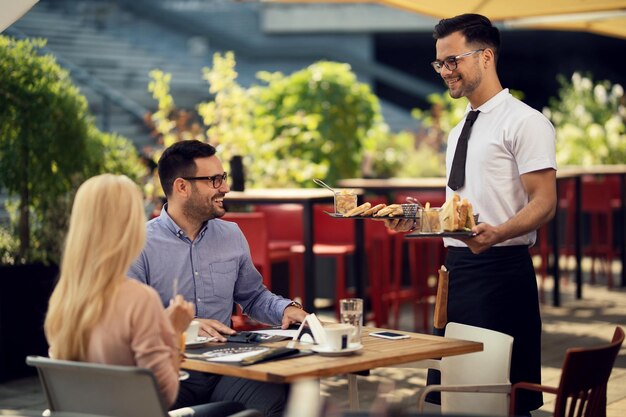 Camarero feliz sirviendo una comida a una pareja durante la hora del almuerzo en un restaurante