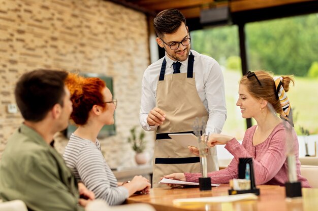Camarero joven que muestra el menú en el panel táctil a sus clientes en un café