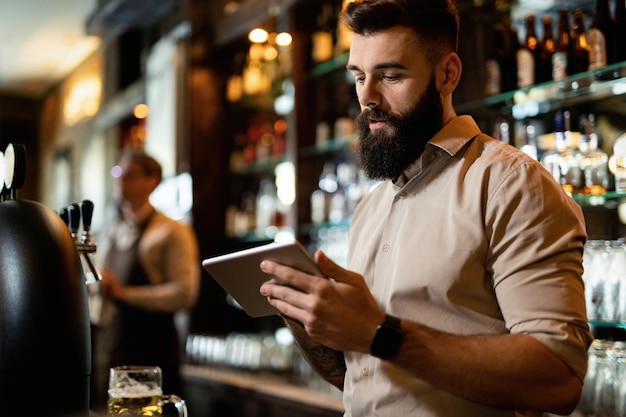 Camarero joven que usa una tableta digital mientras trabaja en un pub
