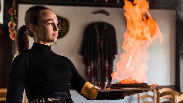 Camarero llevando plato con carne en fuego