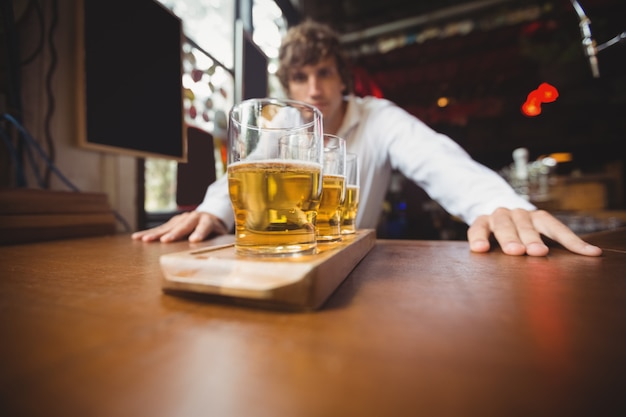 Camarero de pie cerca del mostrador con vasos de cerveza